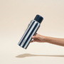 Hand holding a striped water bottle with a blurred plant background