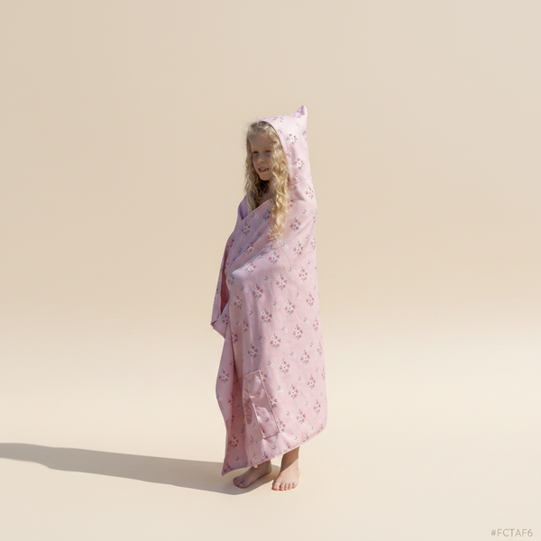 Person wrapped in a pink hooded towel on a sandy beach with ocean and dunes in the background