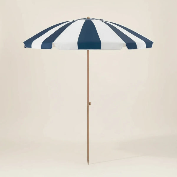 Navy and white striped beach umbrella with a wooden pole on a beige background